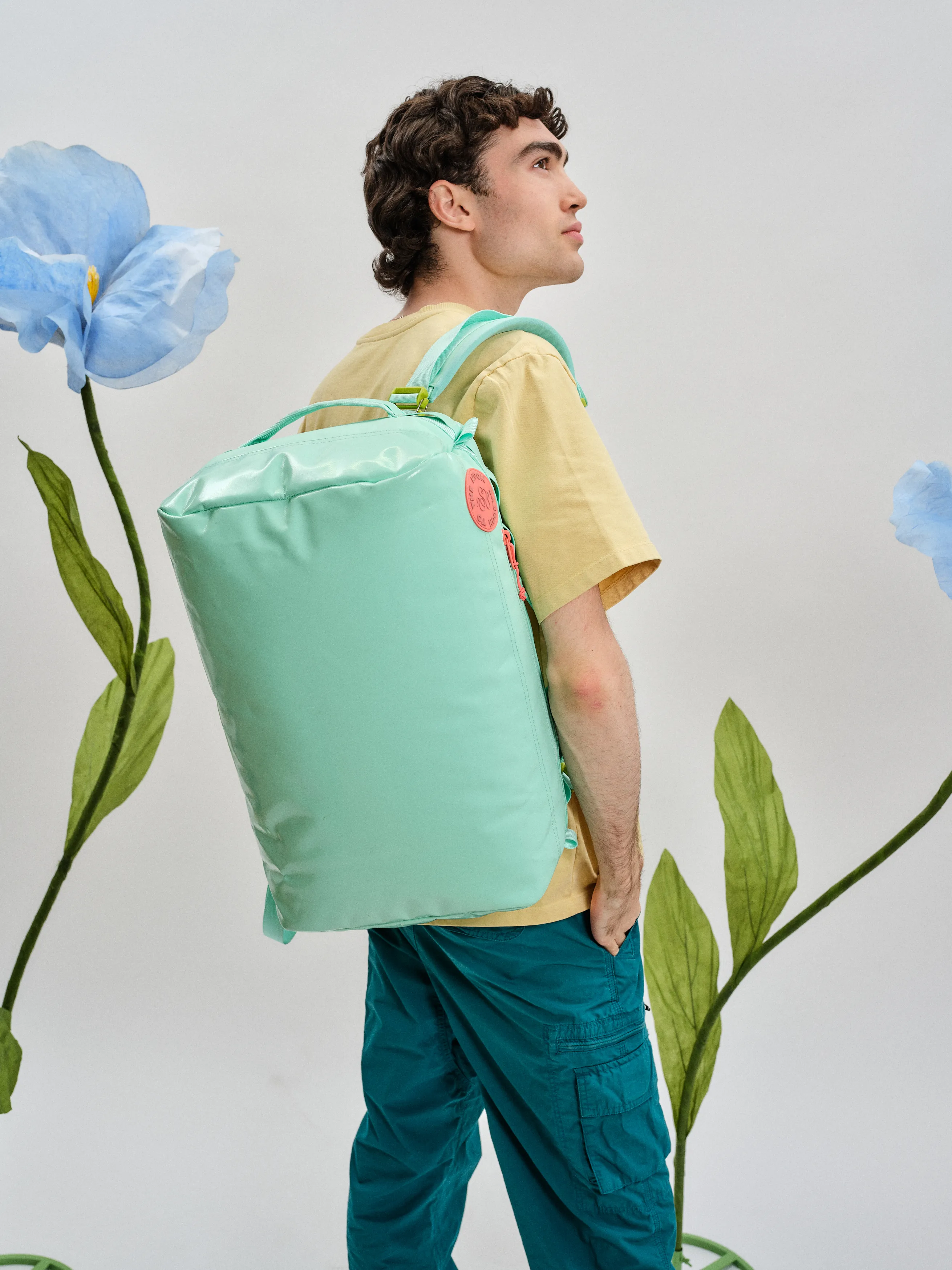 Lachlan wearing a backpack by one strap with flowers behind