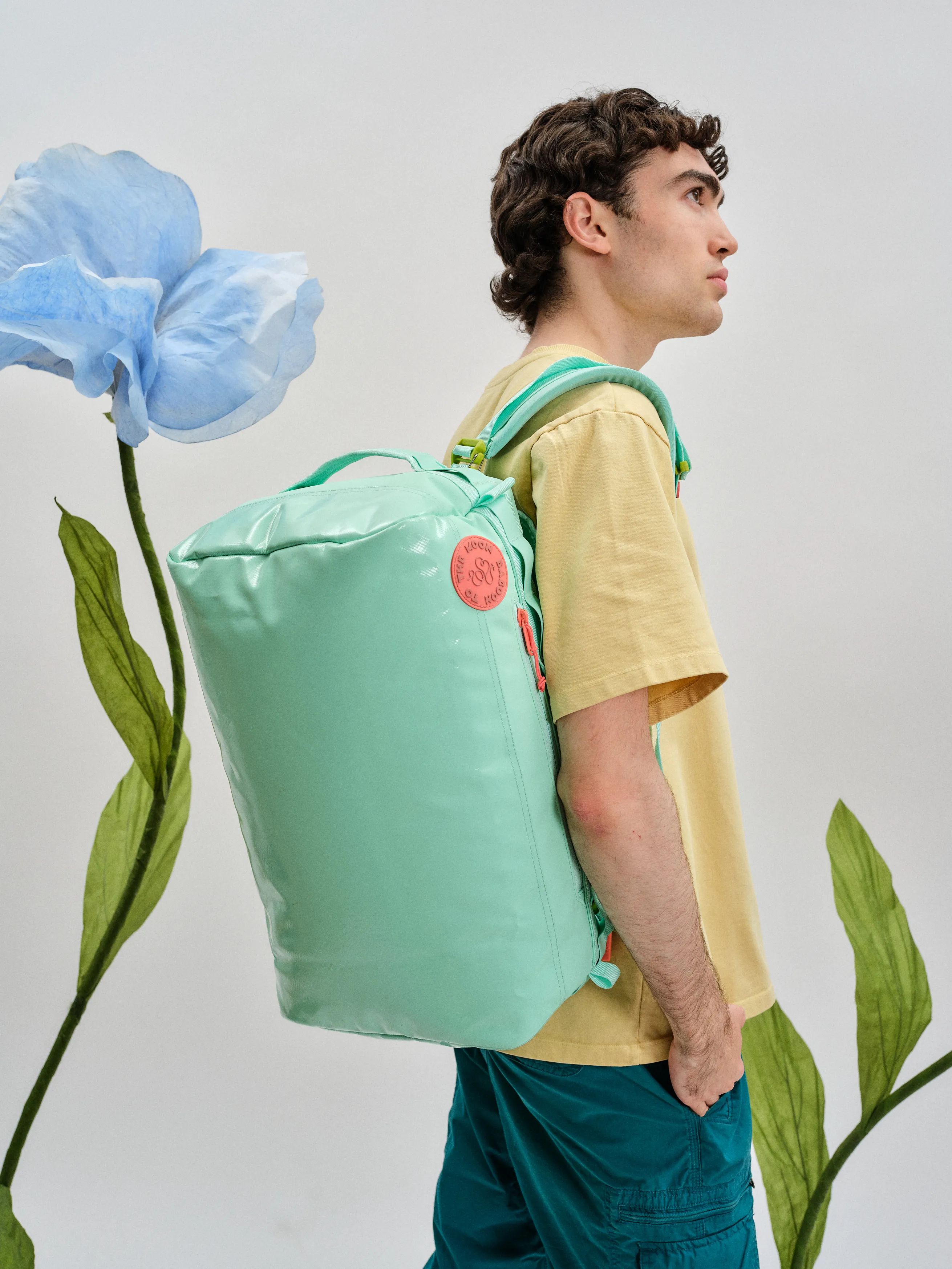 Lachlan wearing a backpack by one strap with flowers behind