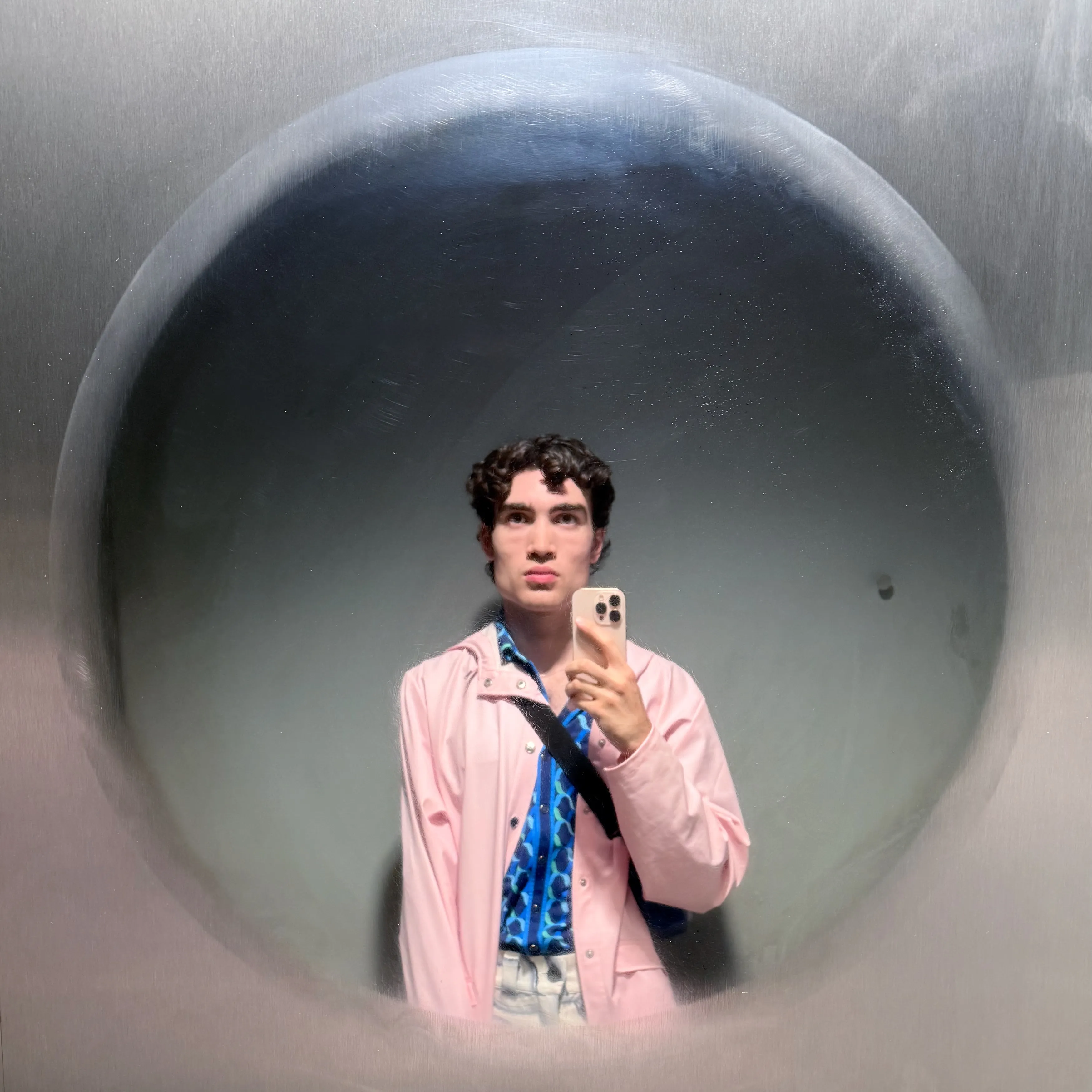Mirror selfie of Lachlan wearing a pink raincoat in a circular mirror seamlessly blending into stainless steel